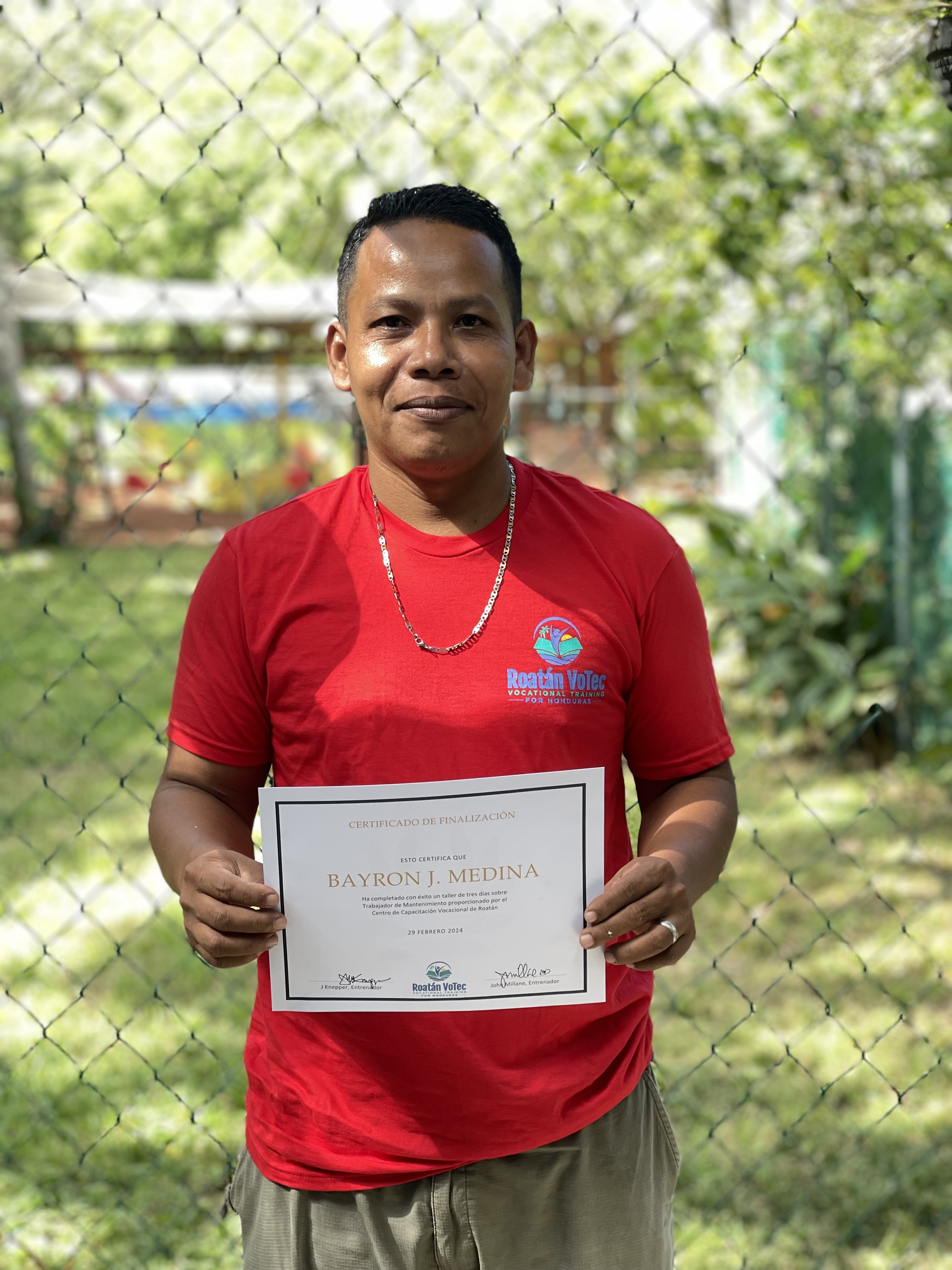 Bayron J. Medina holding his RVT vocational training certificate at graduation in Roatán, Honduras