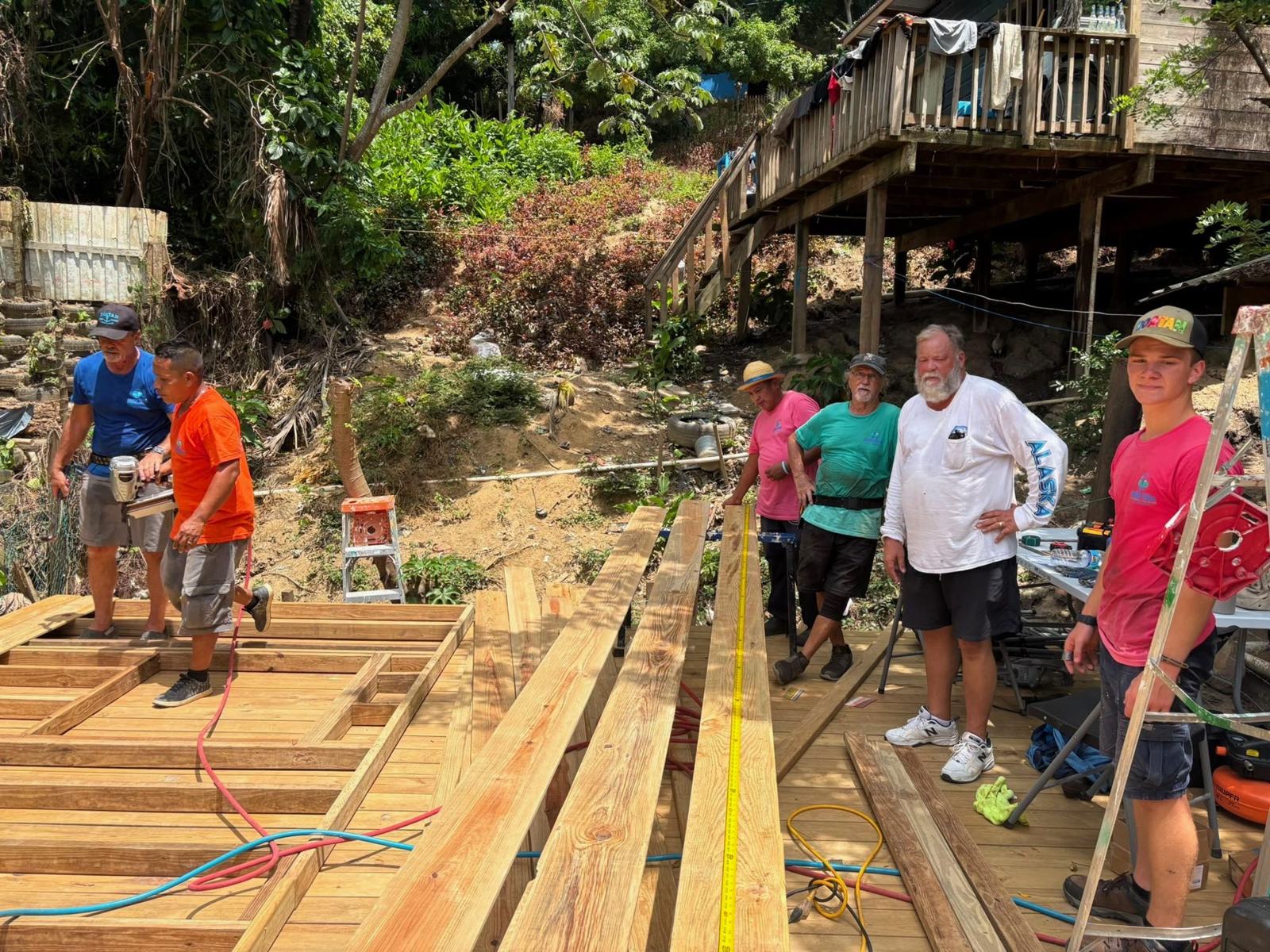 Team members stand on the deck framing at the hillside site