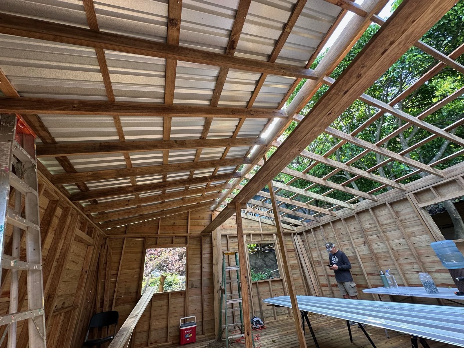 Metal roof panels going on over the roof framing, seen from inside the home with the crew at work below
