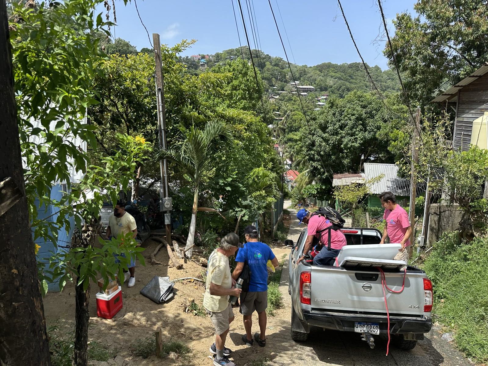 Volunteers load tools into a pickup truck on a narrow hillside road