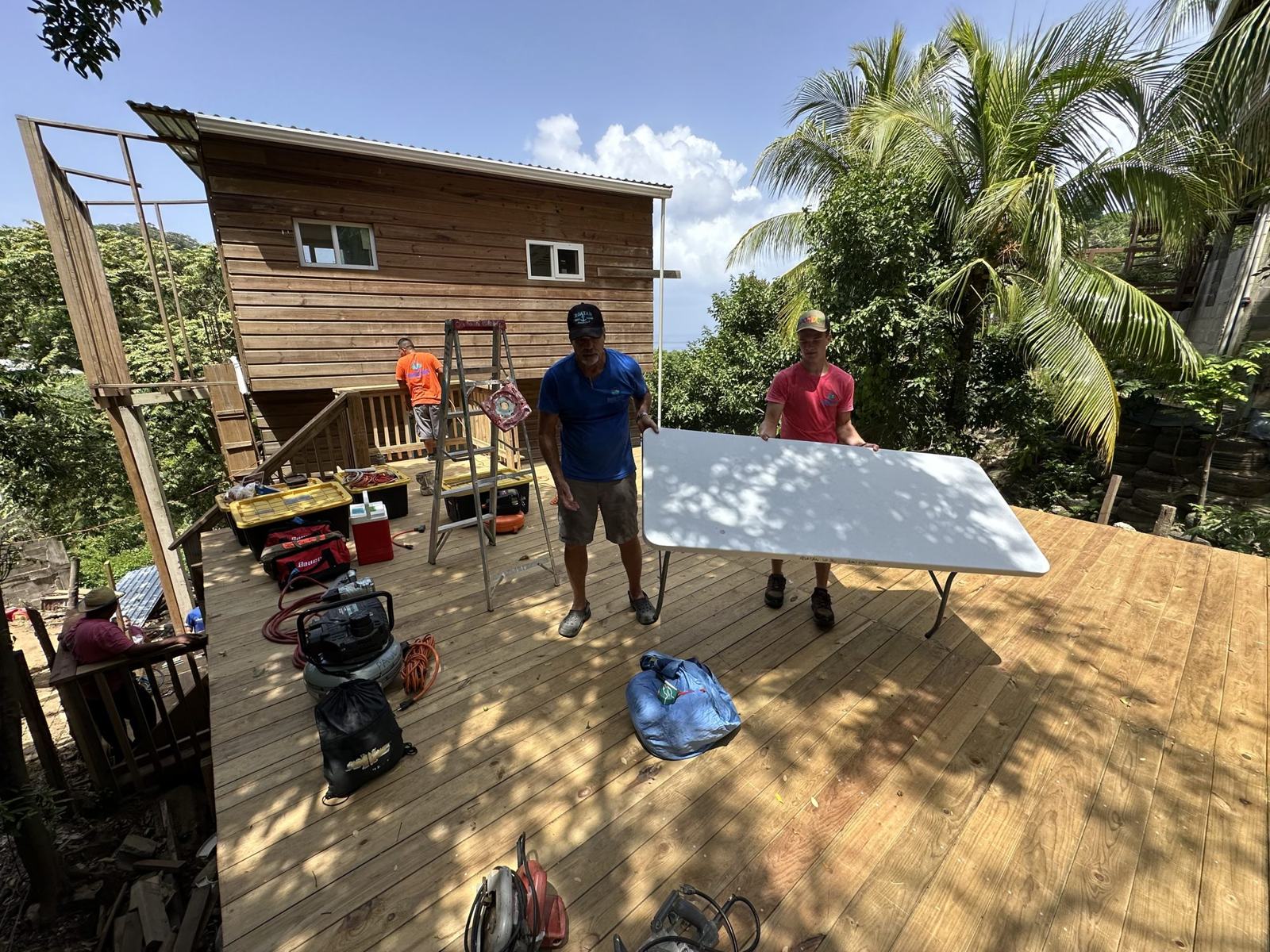 Two builders carry a folding table across a new wooden platform