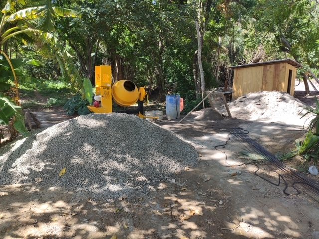 Yellow cement mixer beside piles of gravel and rebar — the concrete slab begins